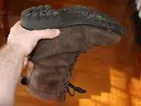 A hand holding a brown work-boot upside down.