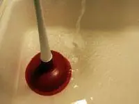 A plunger in a sink with water running.